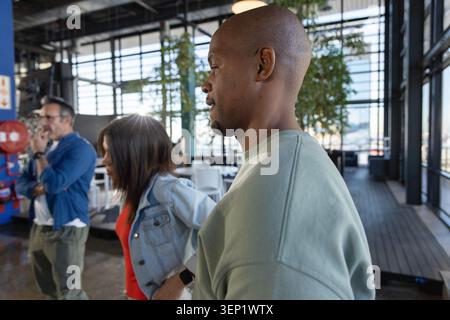 Diverse colleagues walking in communal space by windows, wearing light green sweatshirt Stock Photo