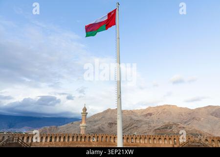 Nizwa Fort with Omani flag after rain under cloudy sky, showcasing national identity, heritage architecture, and cultural tourism Stock Photo