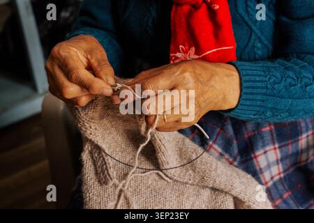 Elderly woman carefully knitting an intricate pattern using wool yarn and circular needles, creating a handcrafted sweater, symbolizing tradition, pat Stock Photo