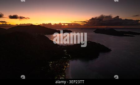 A warm golden sky illuminates the horizon as distant islands rest peacefully beneath the setting sun. Praslin, Seychelles. Stock Photo