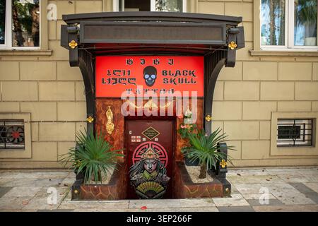 Batumi, Georgia – June 9, 2026: An atmospheric entrance to  tattoo parlor featuring a red sign with a skull image, design on the door, and small palms Stock Photo