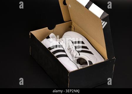 Close up view of Adidas white sneakers in open shoe box isolated on black background. Sweden. Stock Photo