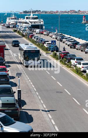A bright day in Zadar showing a public bus driving along a coastal road filled with parked vehicles and a sea view. Stock Photo