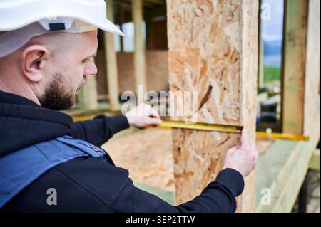 Construction professional checking dimensions of window or door opening in wooden panel, inspecting placement and build precision Stock Photo