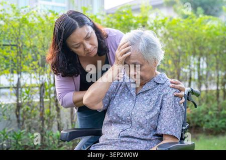 Asian elderly woman headache while sitting on wheelchair at park, healthy strong medical concept. Stock Photo