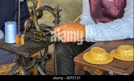 Soulac-sur-Mer, France - June 06, 2026. Close-up of a craftsman sewing miniature straw hats using a vintage mechanical sewing machine during the Soula Stock Photo