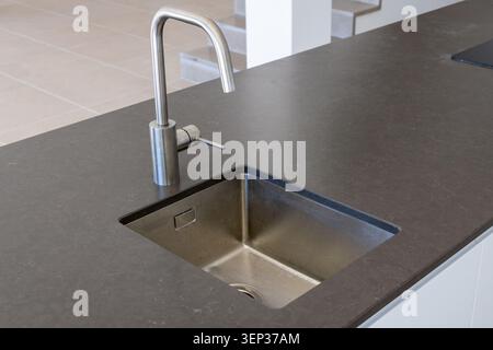 A contemporary kitchen island features a deep stainless steel sink and a minimalist chrome faucet, perfect for a modern home design Stock Photo