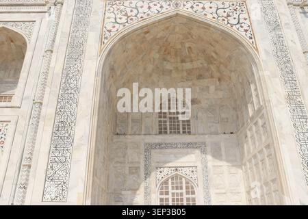 Midday close-up of Taj Mahal white marble showing intricate floral pietra dura stone inlays, relief carvings, and elegant Arabic calligraphy details. Stock Photo