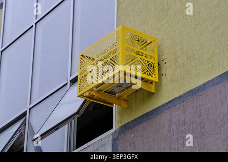 Modern building facade featuring bright yellow air conditioner cage decorated with ethnic patterns Stock Photo