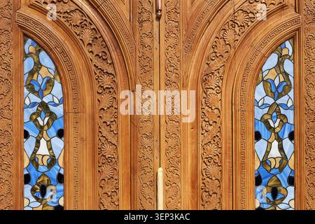 Carved wooden door with stained glass windows in Uzbekistan. Traditional oriental ornament on antique wood. Architectural detail of historical building in Central Asia culture. Stock Photo