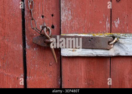 Rusty iron door latch on a weathered red wooden shed door, showing traditional craftsmanship, age and rural Scandinavian heritage Stock Photo