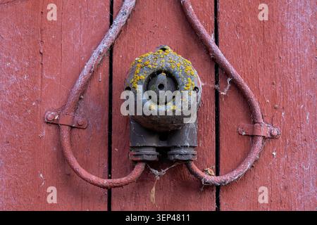 Vintage electrical switch mounted on a weathered red wooden wall, showing signs of age, rust and historical rural craftsmanship Stock Photo