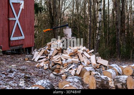 Chopped firewood and axe in a chopping block beside a traditional red wooden shed in rural Norway Stock Photo