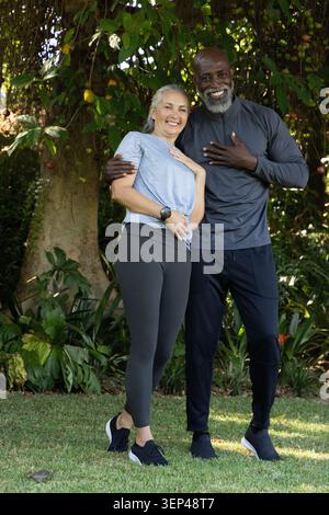 Couple standing smiling on lawn under tree with vines in athletic wear with watch and sneakers Stock Photo