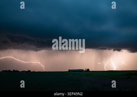 Dramatic lightnings strike over rural field under dark thunderstorm clouds at dusk Stock Photo