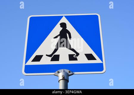 Close-up of a blue pedestrian crossing traffic sign against a clear blue sky. Road safety symbol marking a zebra crossing for pedestrians. Stock Photo