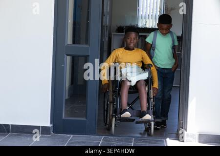 Two African American school-age boys entering school room with wheelchair, backpacks, mustard shirt Stock Photo