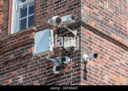 Multiple CCTV security cameras installed on the corner of a red brick building, representing urban surveillance, monitoring, and safety infrastructure Stock Photo