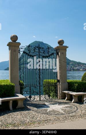 Beautiful vertical scenic view of Lake Lugano and Monte San Salvatore mountain through the ornate historic wrought iron gate of Parco Ciani public par Stock Photo