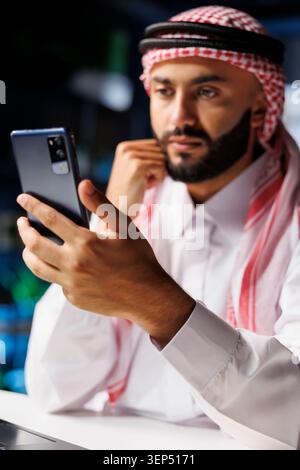 Close-up shot of Middle Eastern male adult holding his cell phone for a video conference call. Detailed view of a youthful Muslim man surfing the net on his digital mobile device. Stock Photo
