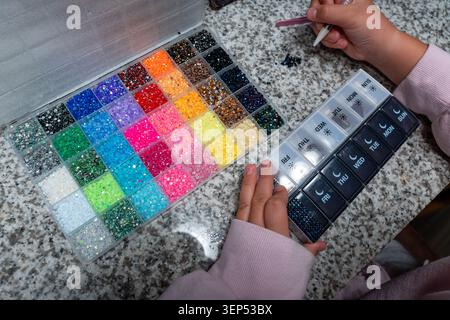 Close-up of children’s hands applying rhinestones in a bedazzling craft activity. Creative DIY hobby for kids, focused on decoration, imagination Stock Photo