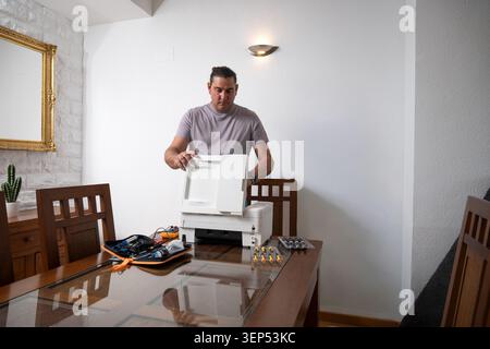 Man opening a printer for maintenance on a dining table with various tools Stock Photo