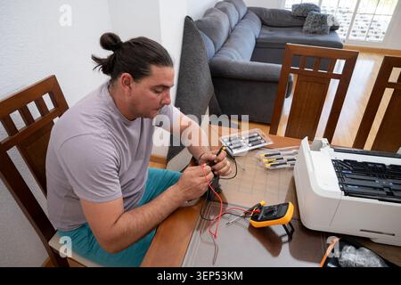 Man troubleshooting and fixing an office printer with a multimeter at home Stock Photo