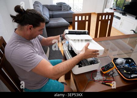 Man troubleshooting and fixing personal printer at home using various tools Stock Photo