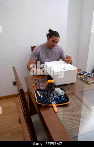 Man troubleshooting and repairing a home printer, focused on electronics maintenance Stock Photo