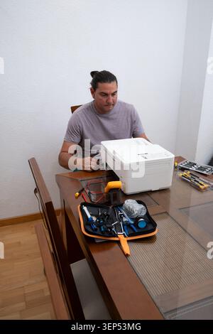 Mid adult man fixing a printer on a table, using various electronic repair tools Stock Photo