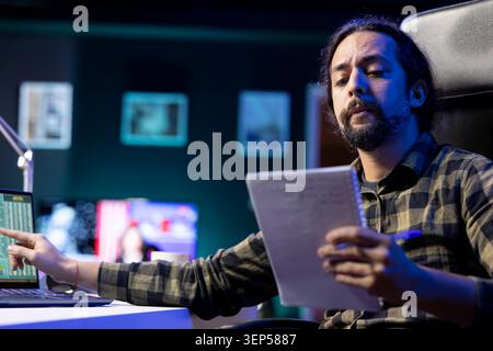 Determined man working diligently at his desk using laptop and pen, researching, and brainstorming ideas. Productive and focused male individual utilizing notebook and technology for work and study. Stock Photo