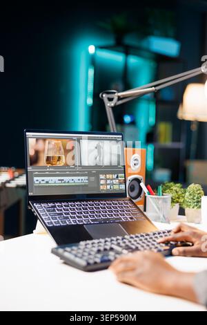 Black person working from home, immersed in her creative work while she uses digital laptop and editing software, typing on the keyboard. Stock Photo