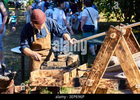 Artisan in period clothing demonstrating an ancient craft, skillfully manipulating coals at a sunlit outdoor festival. Historical reenactment scene: R Stock Photo