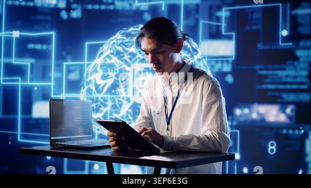 Productive engineer in high-tech workspace uses artificial intelligence computing simulating human brain, admin in server farm running operations on laptop with AI machine learning algorithms. Stock Photo