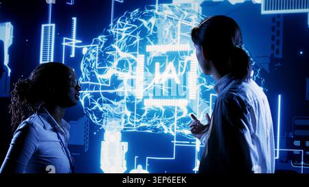 African American engineer and Asian coworker looking at hologram of artificial intelligence human brain simulation, BIPOC IT team members interacting with AR AI visualization. Stock Photo