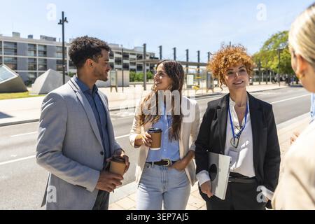 Diverse business professionals having an informal outdoor meeting on a sunny city street, walking and chatting over coffee while discussing strategy, Stock Photo