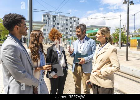 Group of diverse business professionals having an informal meeting and engaging in conversation while standing at an outdoor urban public transport st Stock Photo