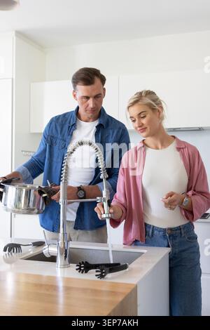 Couple standing at kitchen sink filling stainless steel pot from chrome spring faucet near utensils Stock Photo