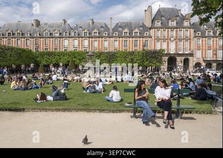 Two young woman talking on a park bench in Square Louis-XIII on the historic Place des Vosges, in the background numerous people relaxing on the lawns Stock Photo