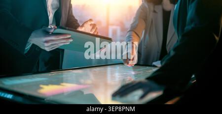 Dynamic image capturing a team of professionals collaborating over a large interactive digital touchscreen table and a tablet, set against a backdrop Stock Photo