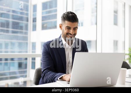 Smiling Indian businessman working remotely on laptop Stock Photo