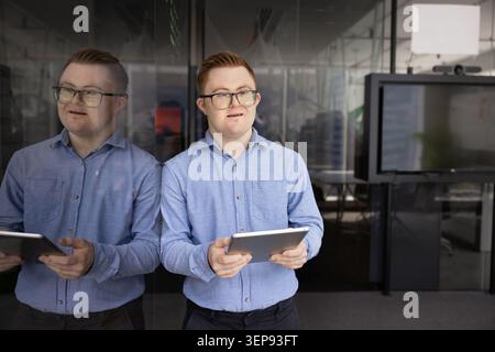 Young man with Down syndrome holding tablet in office Stock Photo