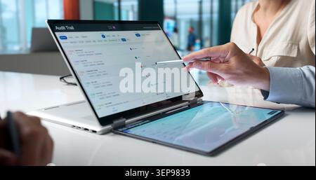Team Members Analyze Digital Compliance Logs Using Laptops In Hybrid Office Setting. Stock Photo