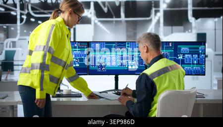 Two Factory Workers Discuss Production Changes During Busy Shift Handover. Stock Photo