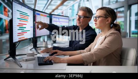 Two Agile Team Members Discuss Project Tasks Using Multiple Computer Screens. Stock Photo