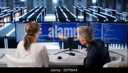 Two Programmers Typing On Computers In Big Data Center Room Managing Servers. Stock Photo
