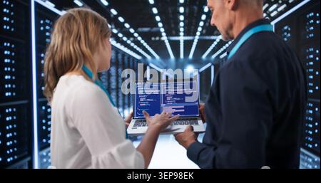 Two Engineers Analyzing Cloud Servers On Laptops In Modern Data Center. Stock Photo