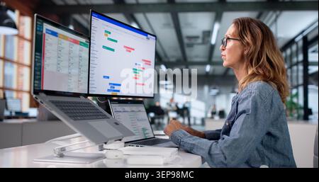 Woman Uses Laptop Reviewing Project Task Schedule And Planning Workflow. Stock Photo