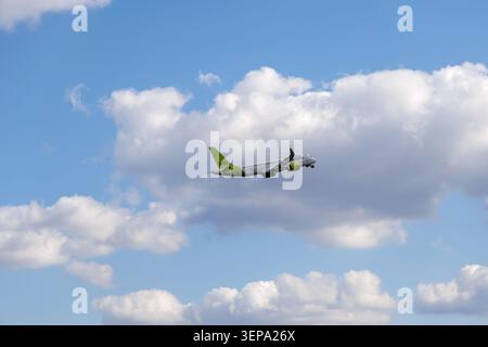 A modern commercial aircraft heading up towards the stratosphere against a brilliant blue sky populated by puffy white clouds. Stock Photo