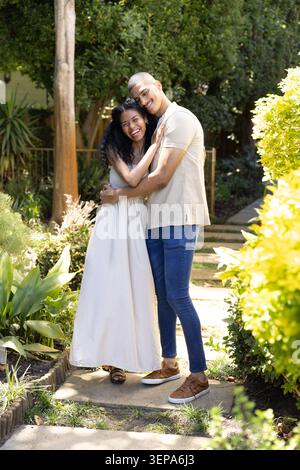African American couple embracing on paved garden path near stone steps, in maxi dress and sneakers Stock Photo